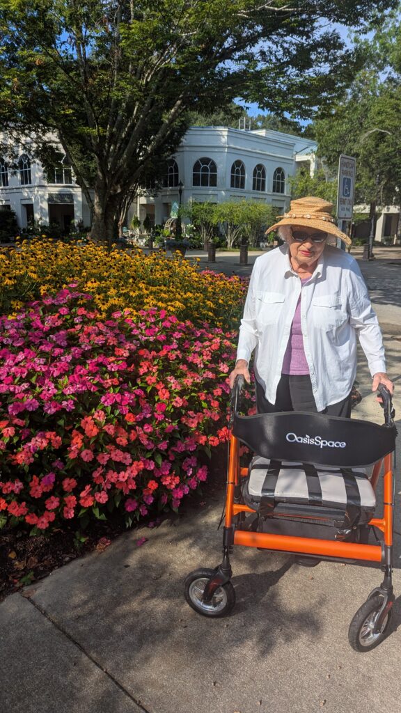 Elderly woman with walker near vibrant flowers.